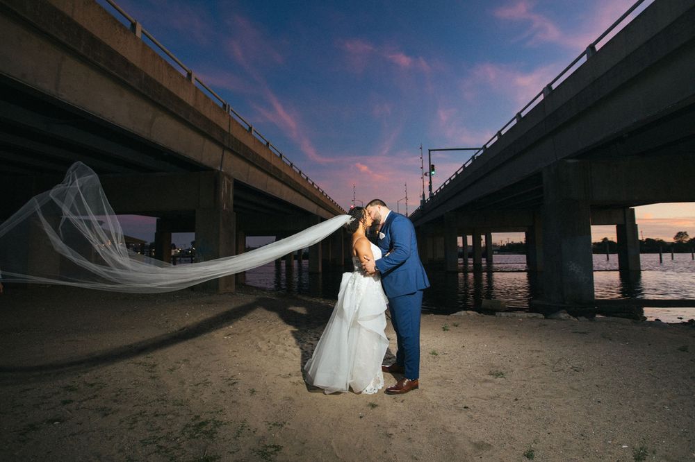A dramatic wedding photo under a bridge at sunset with flowing veil.