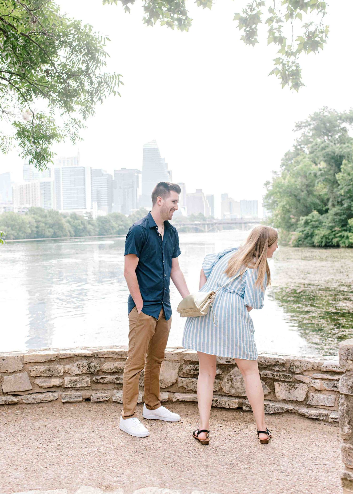 Couple walking along riverside path with city skyline in background.