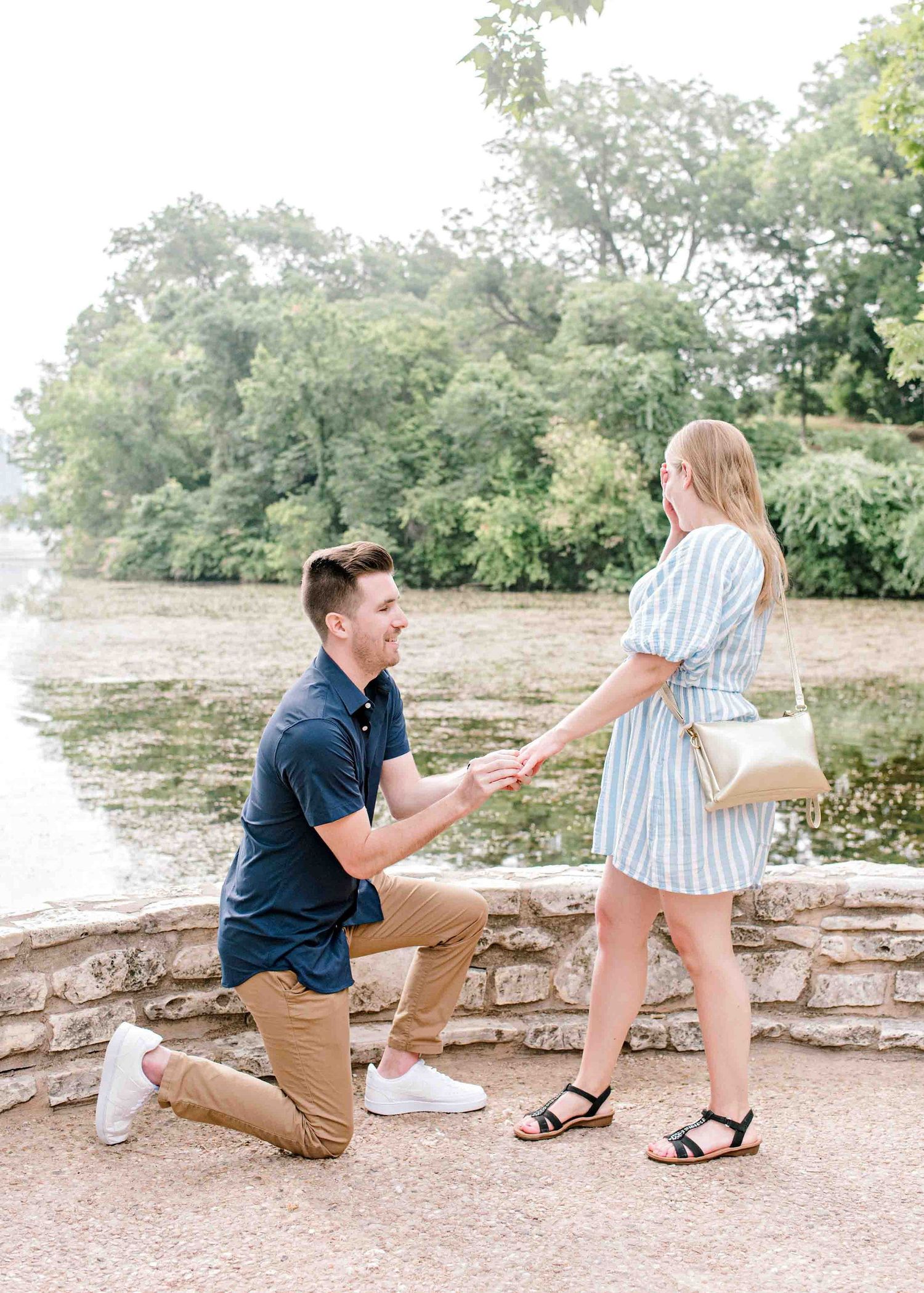 Romantic proposal moment captured by riverside with urban skyline visible.