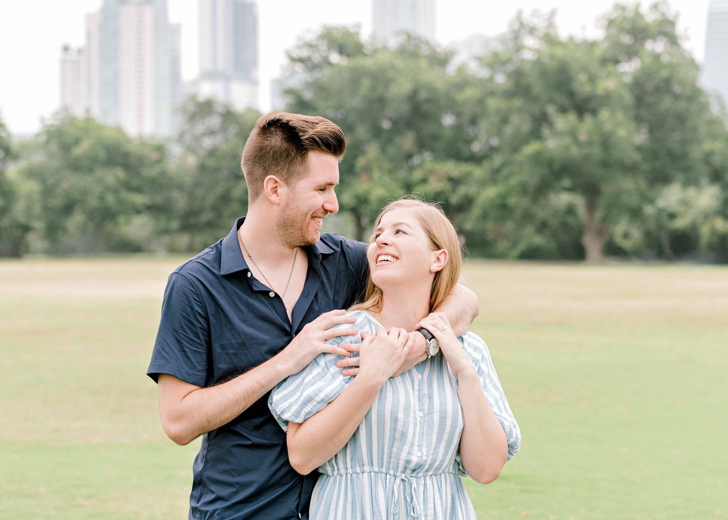 A couple laughs together during their engagement photos with skyscrapers in the background.