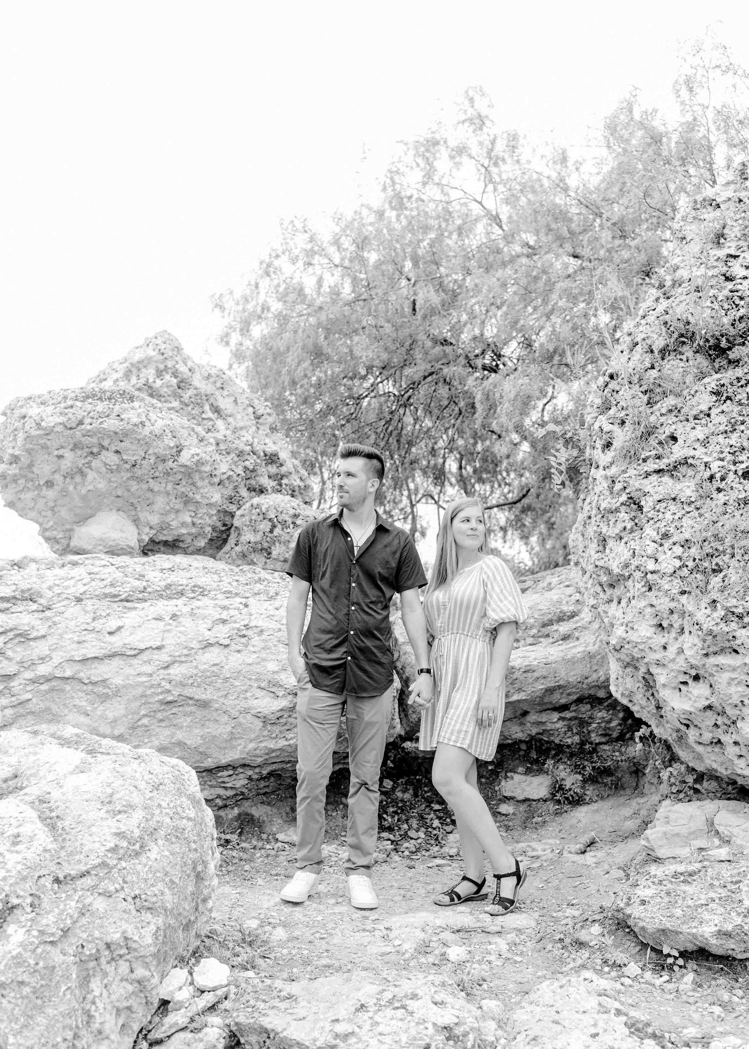 Black and white portrait of a couple posing on rocky terrain surrounded by trees.
