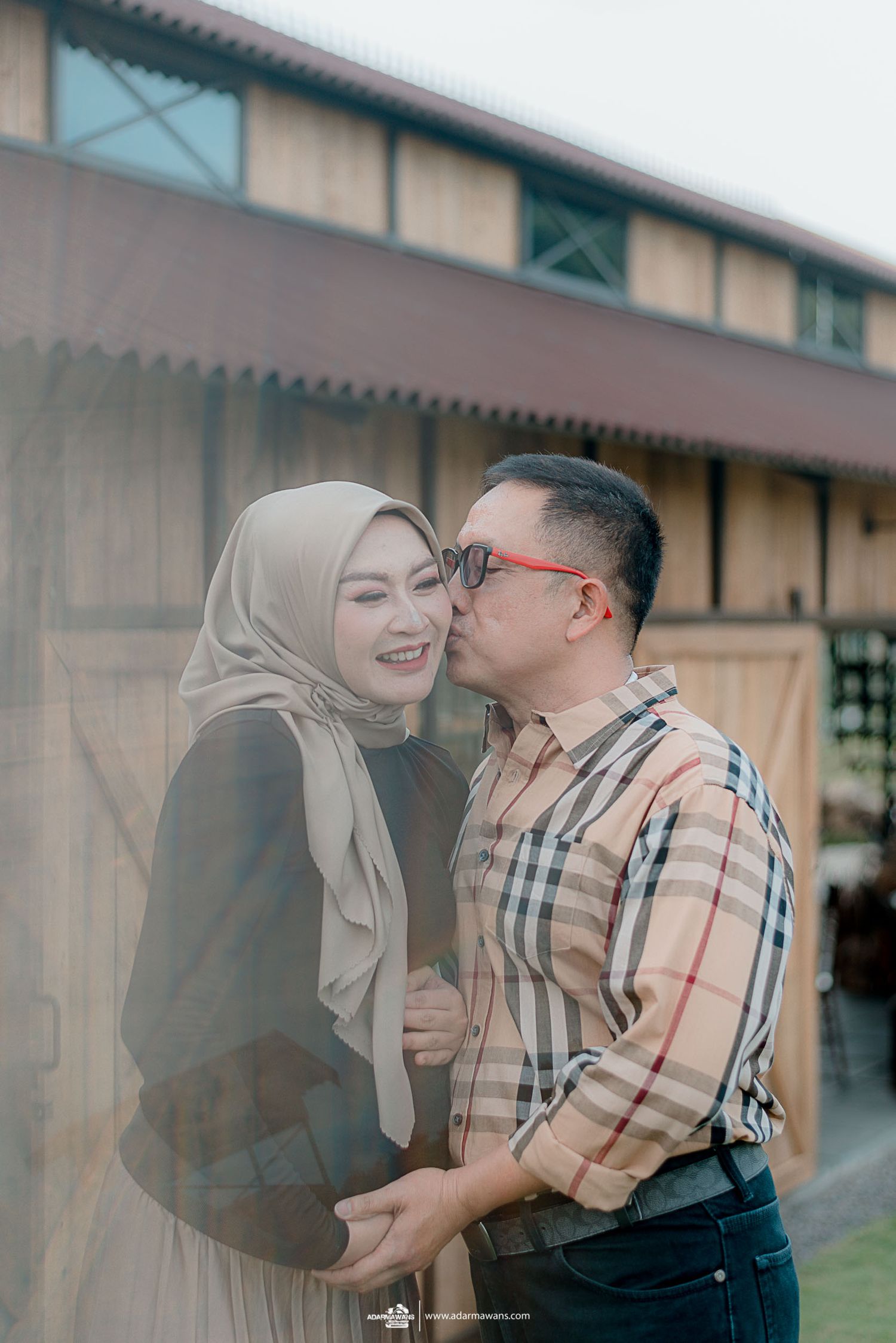 Couple sharing tender moment against rustic building exterior.