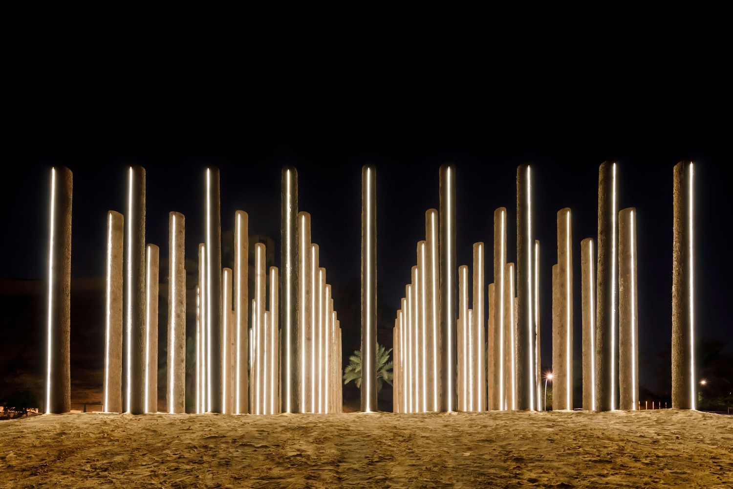 Illuminated vertical light poles arranged in a row create a dramatic nighttime art installation.