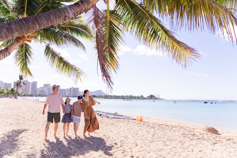 A small group enjoys the sandy beach with palm trees and city skyline in the background.