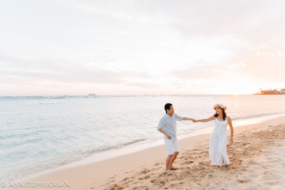 Two people hold hands while walking along a pristine beach at sunset.