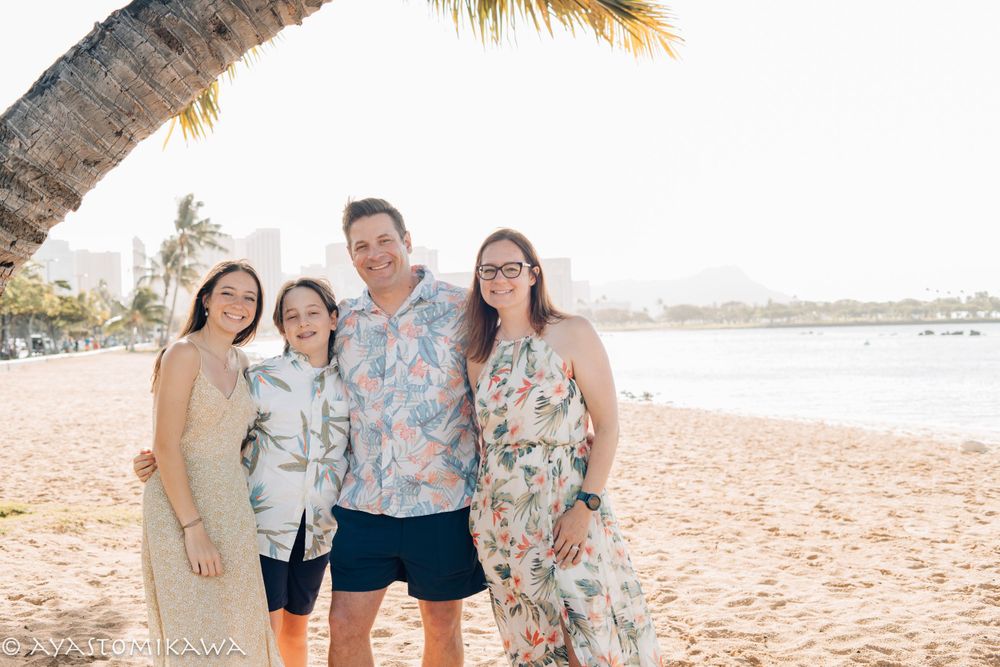 A family poses together on a tropical beach with palm trees and ocean views.