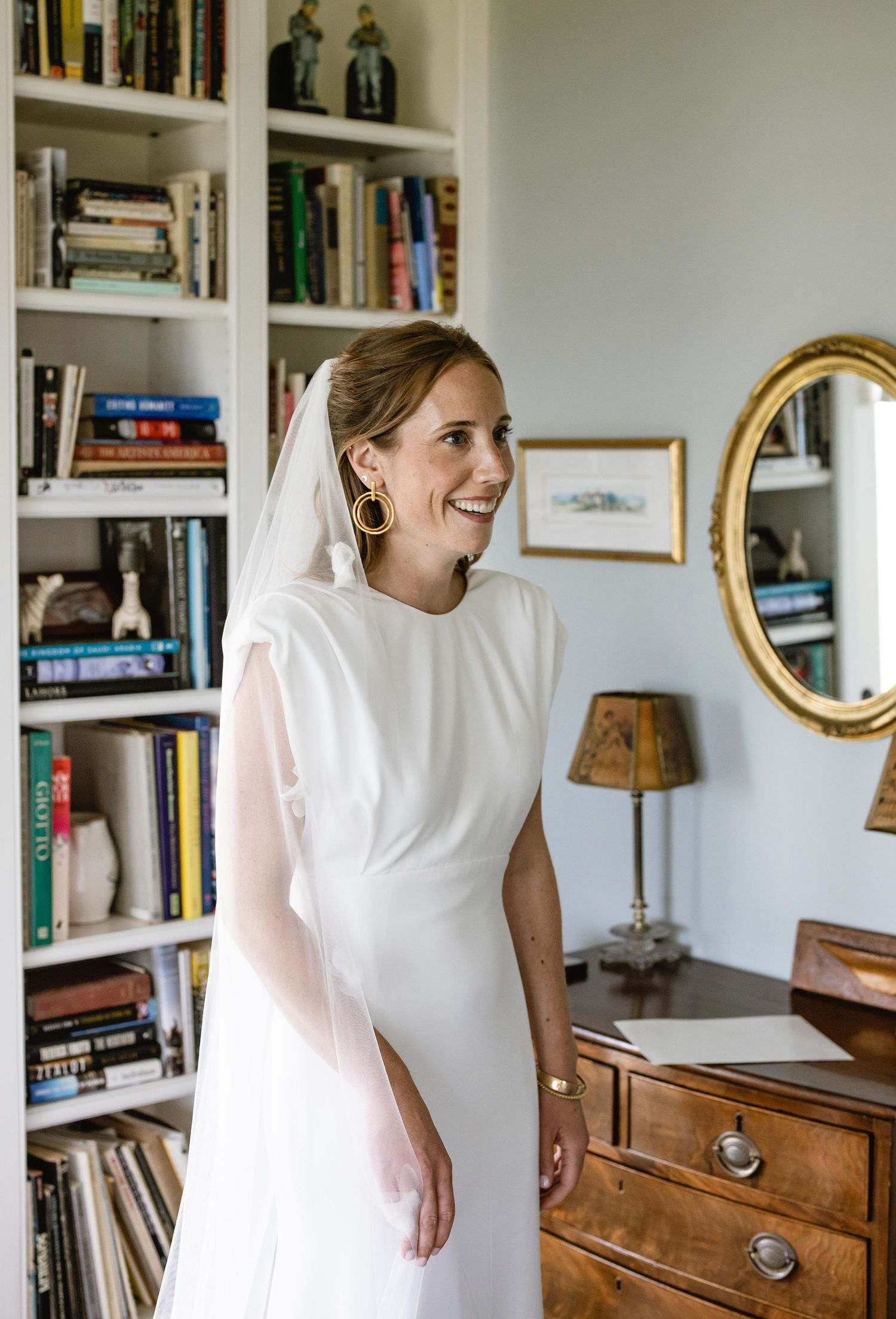 A bright room with bookshelves and a piano where wedding preparations are taking place.