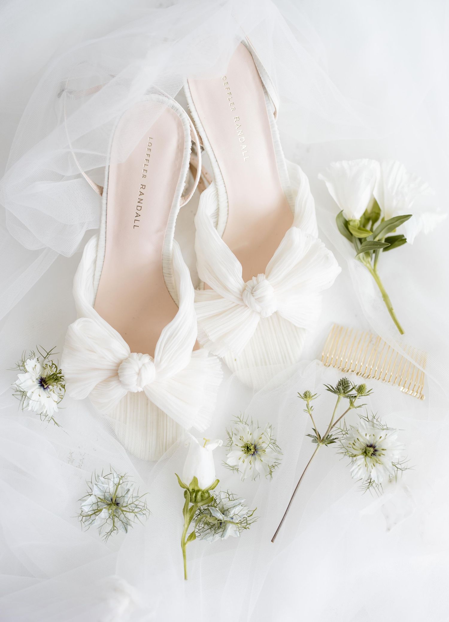 Bridal shoes in blush pink with white floral details on a soft white surface.