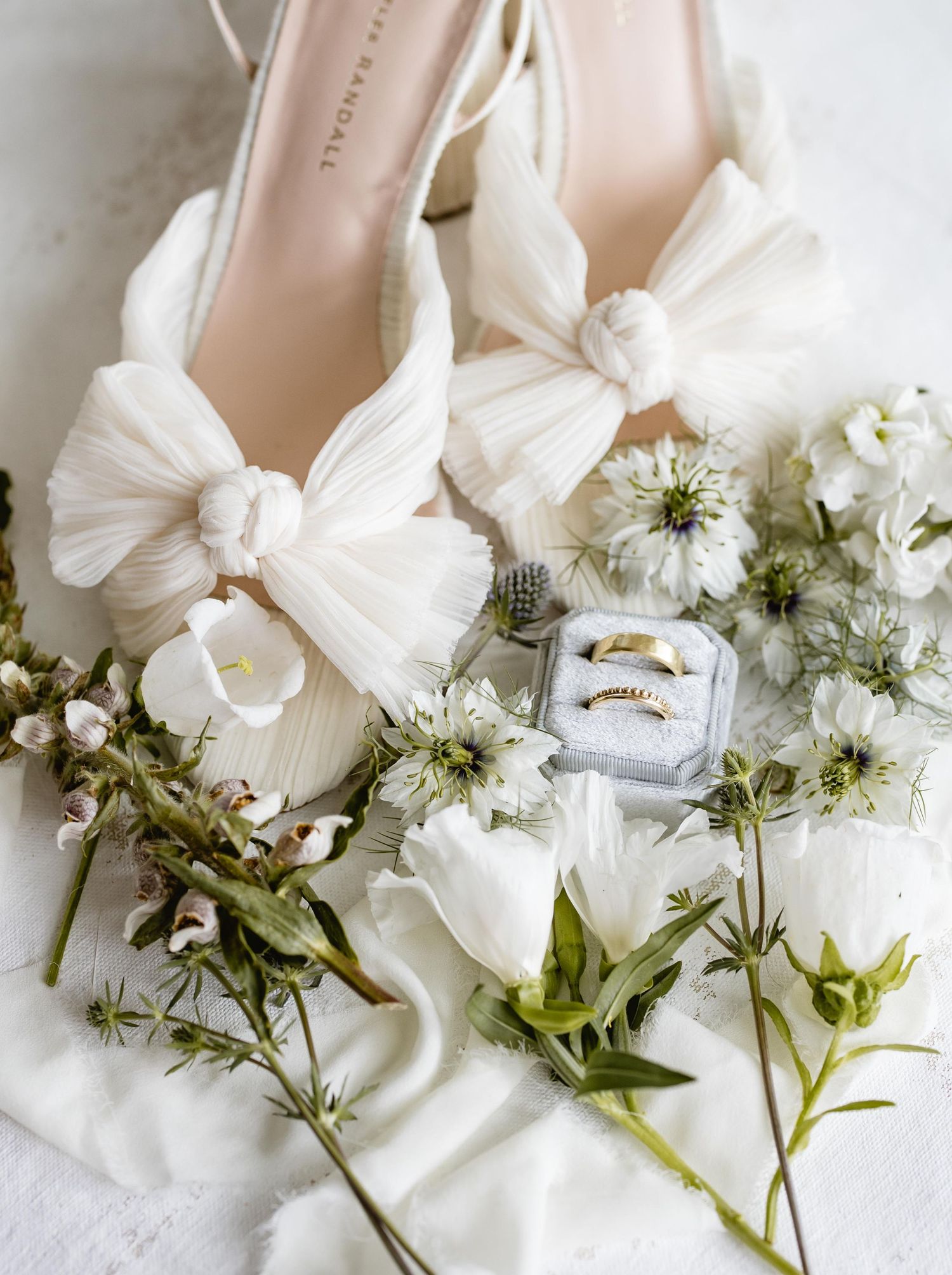 White wedding shoes and delicate flowers arranged on a light background.