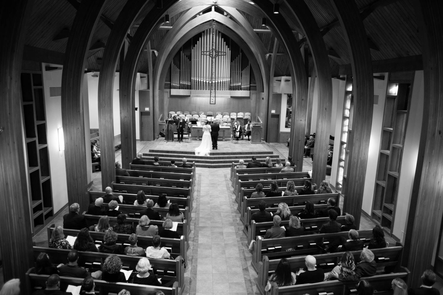 Black and white photo of a church wedding ceremony with guests seated in wooden pews.