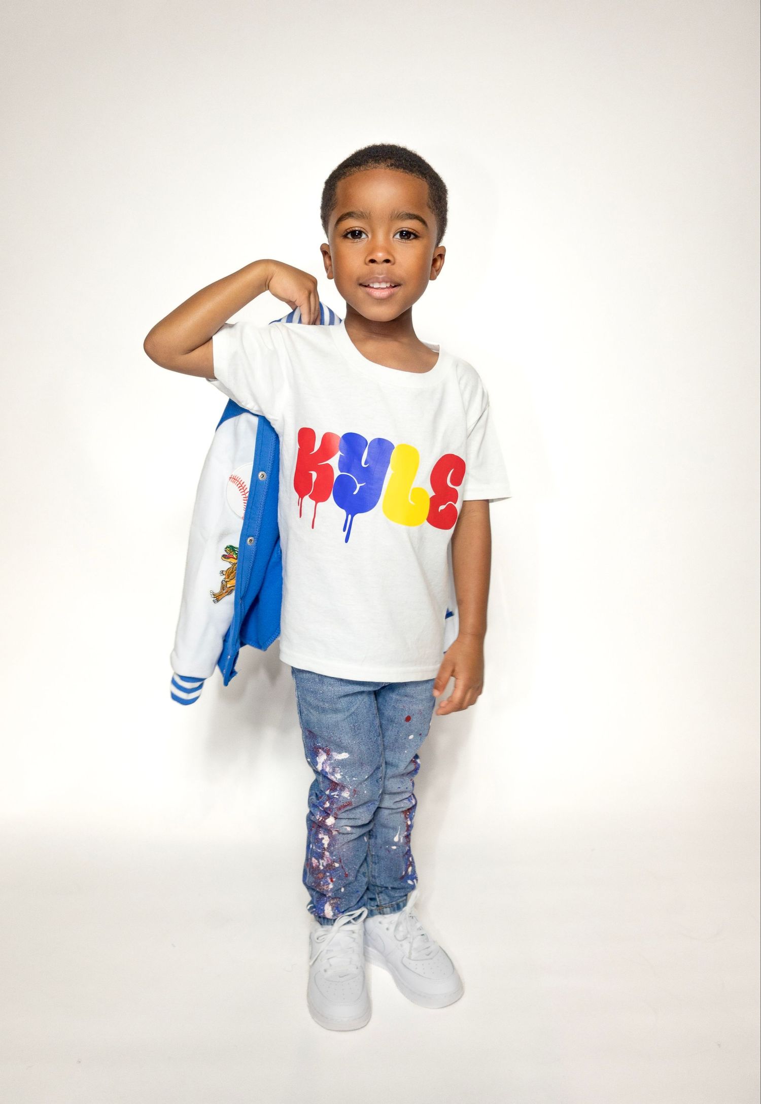 Child wearing white t-shirt with colorful text and distressed jeans against white background.