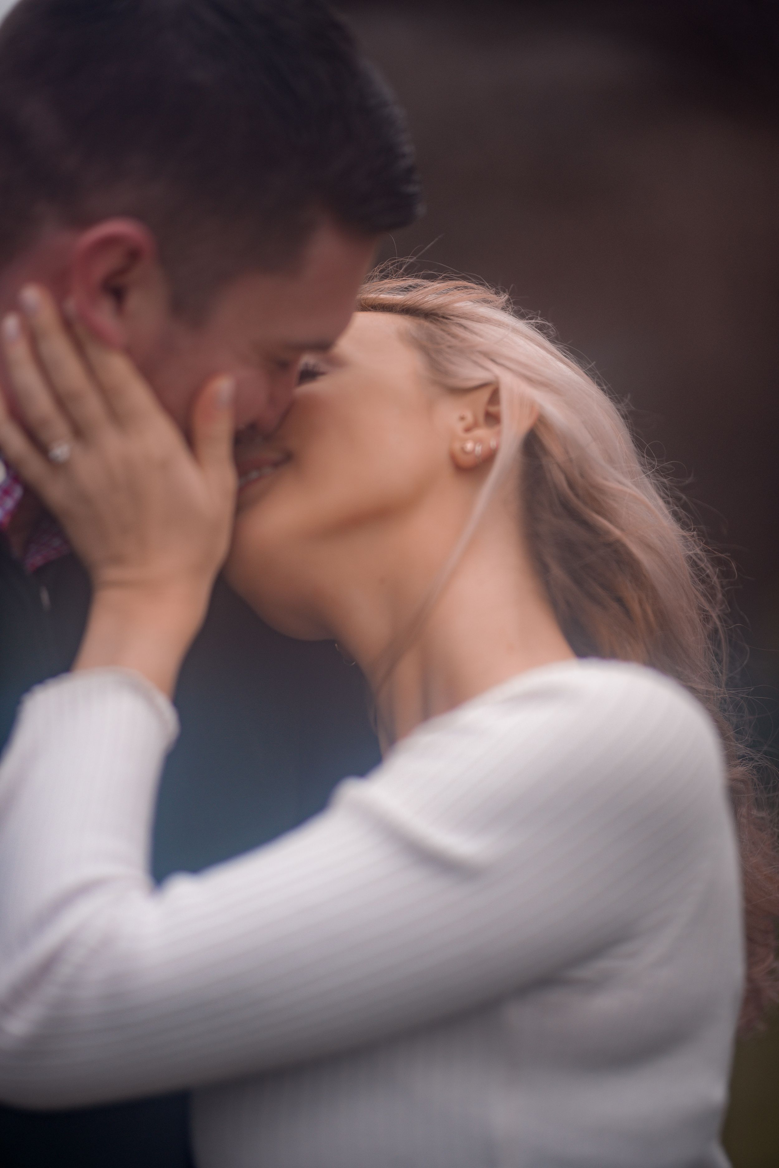 blonde woman passionately kisses her fiance with her hand on his face showing off her engagement ring