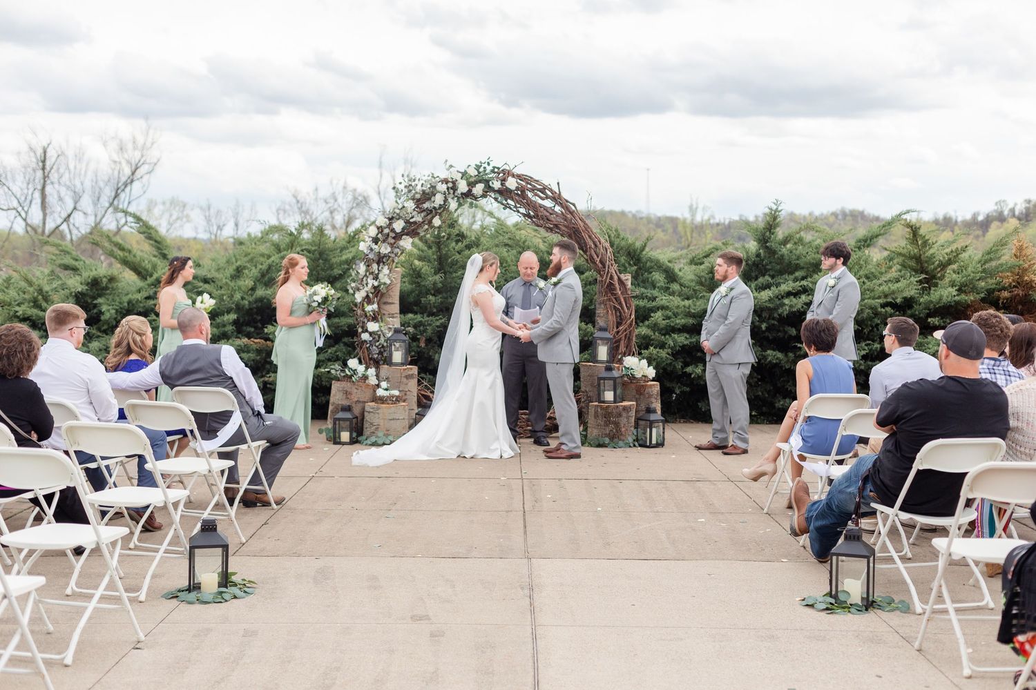 Wedding guests seated in white folding chairs on a stone patio during an outdoor ceremony.