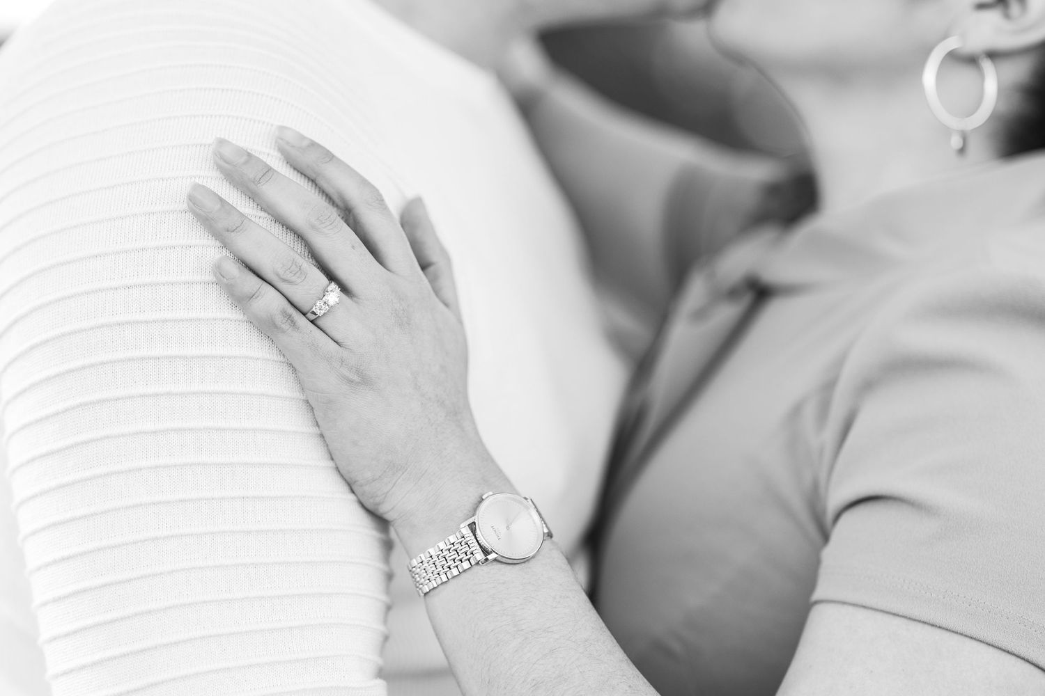 Close-up shot of hands with engagement ring in soft white lighting.