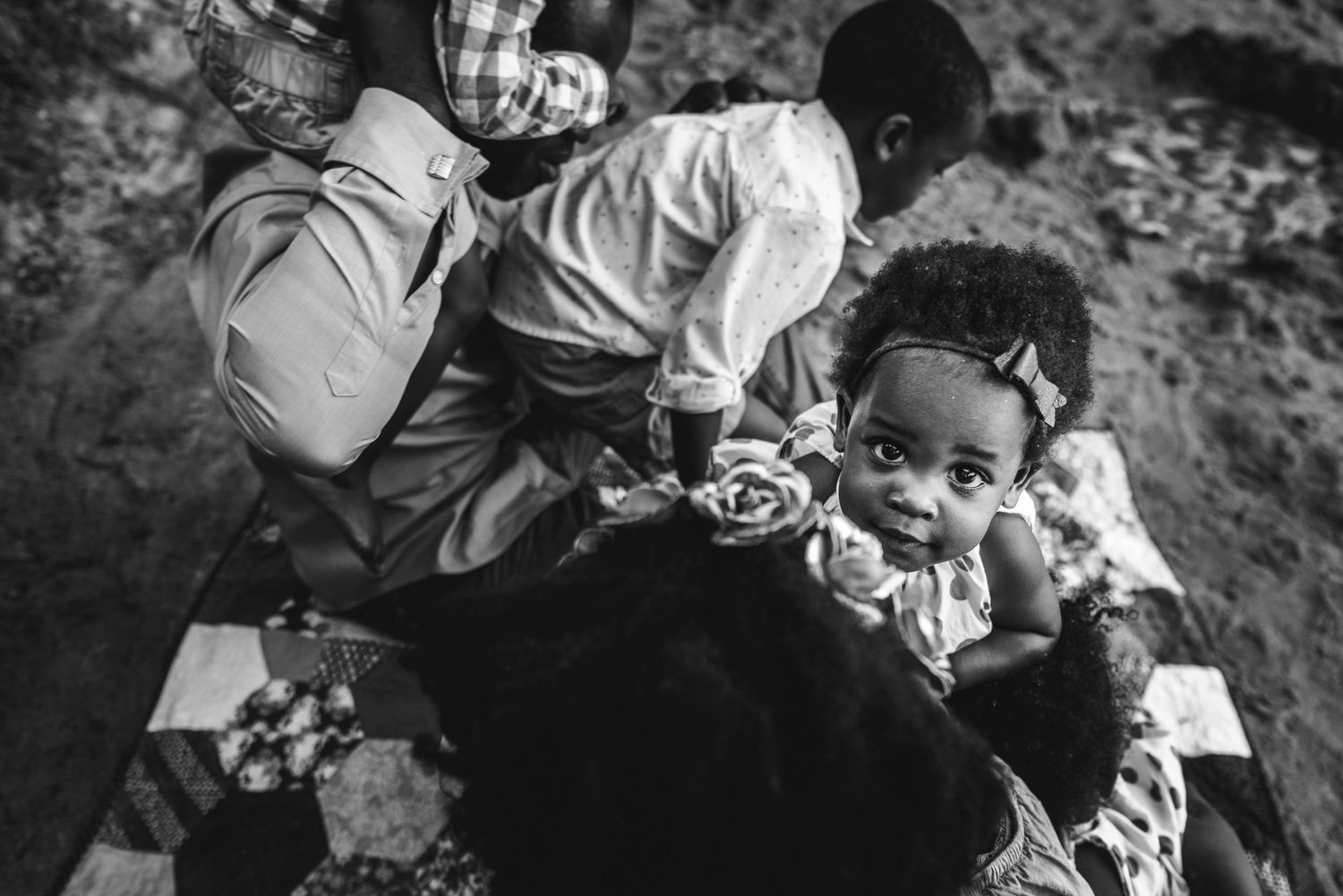 A beautiful little baby with a bow in her hair looks up at the camera as she's held by her mom.