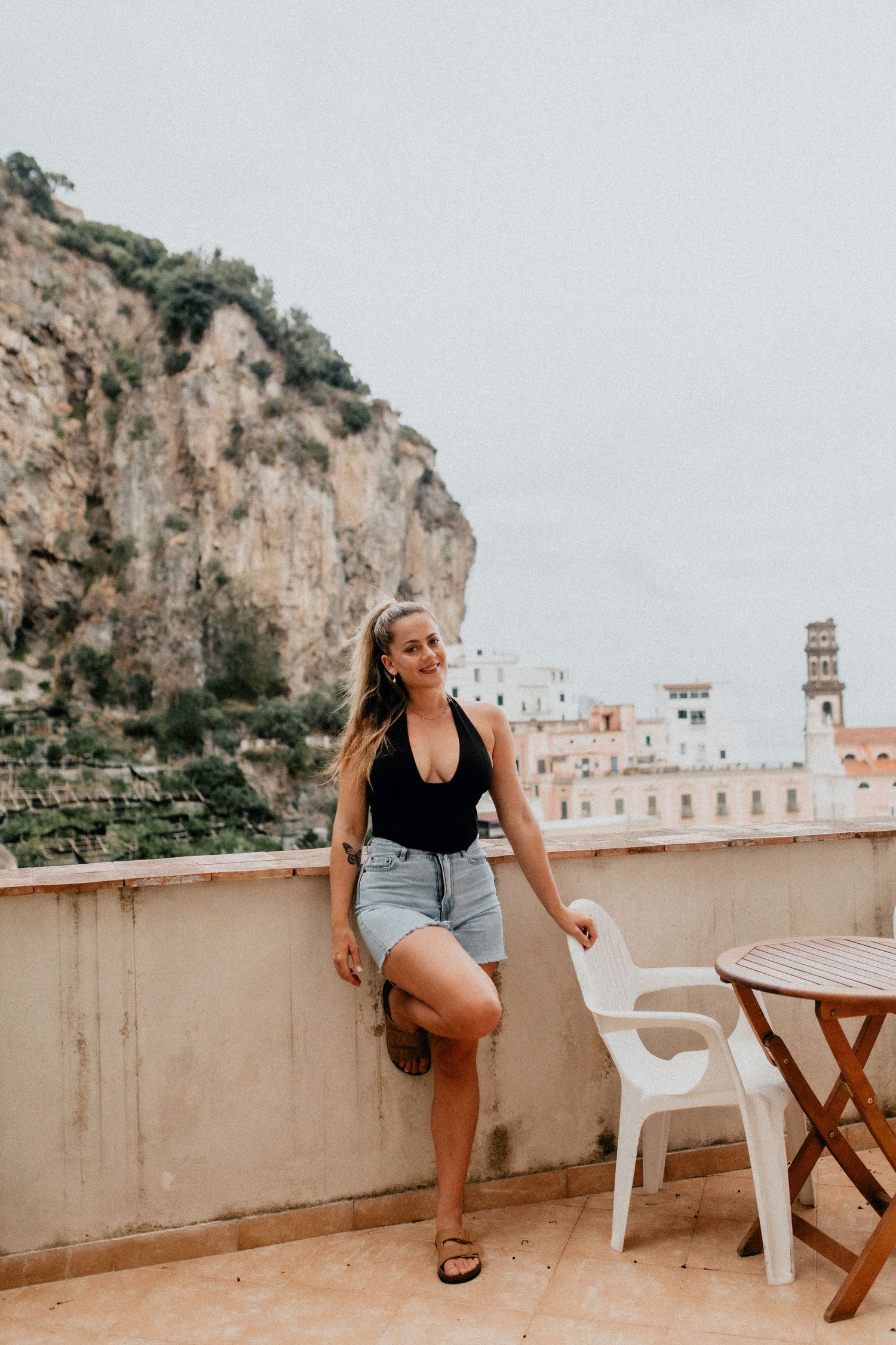 Woman enjoying sunny terrace view of Mediterranean coastal cliffs.