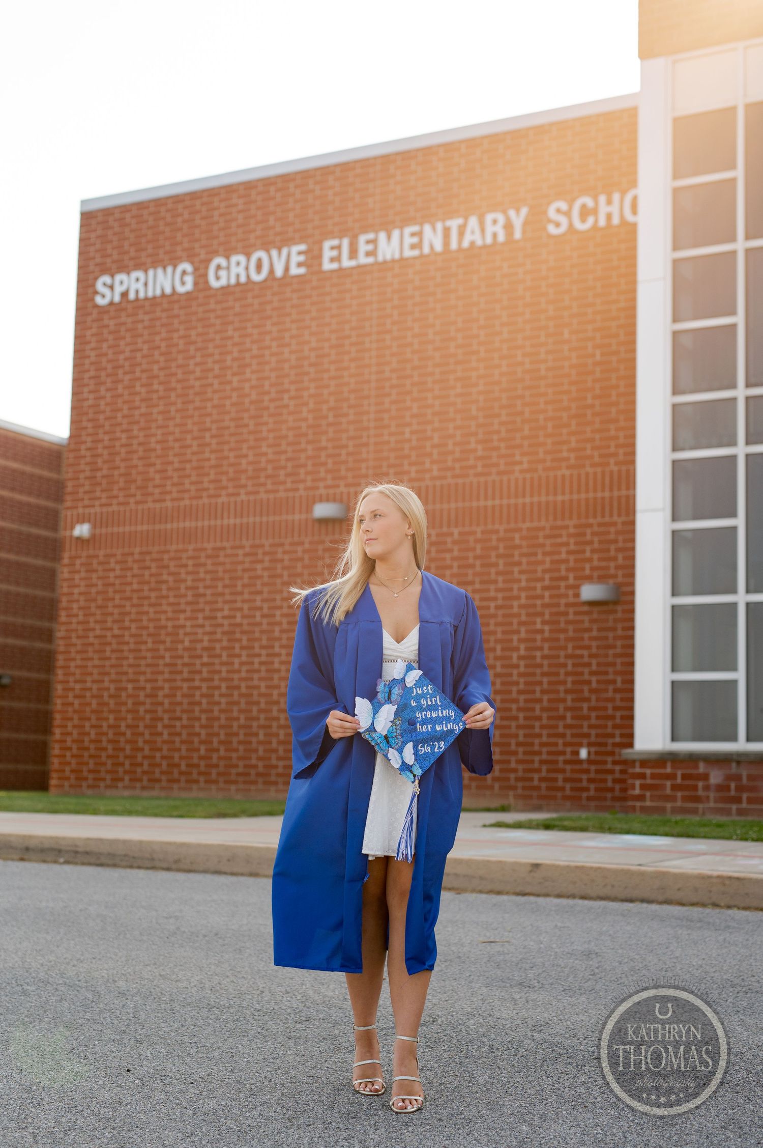 Graduate poses outside Spring Grove Elementary School in blue graduation gown and heels.