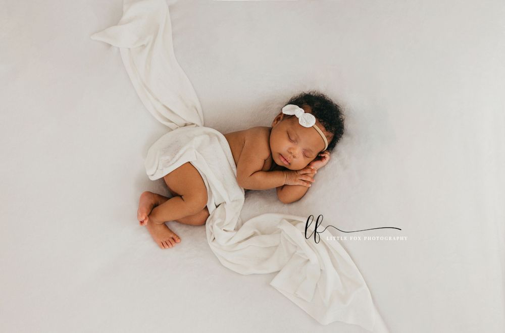 newborn baby girl white backdrop and wrap with a white headband sleeping pose