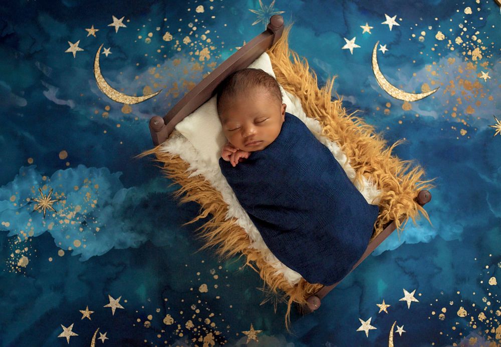 newborn baby boy on a bed with navy and gold star sky backdrop