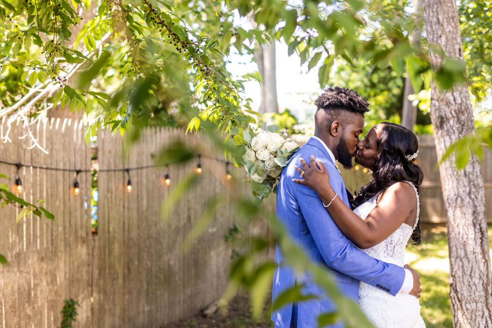 Intimate outdoor moment between couple framed by green leaves and wooden fence.