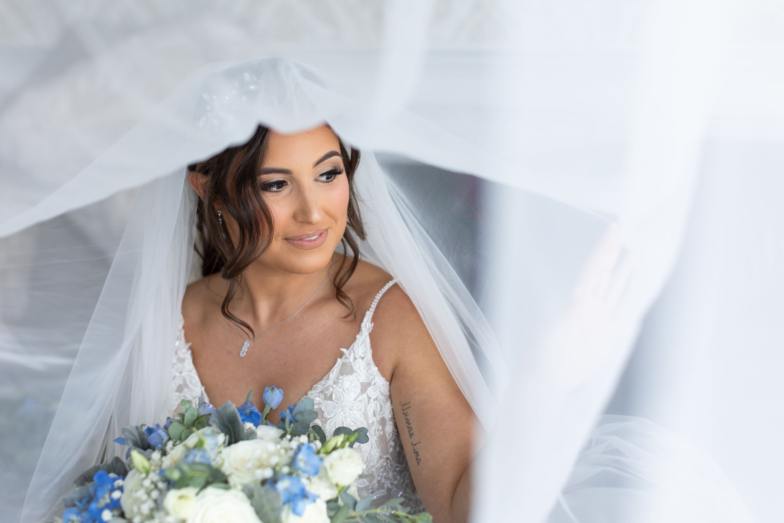 A delicate bridal portrait through white veil with blue and white bouquet.