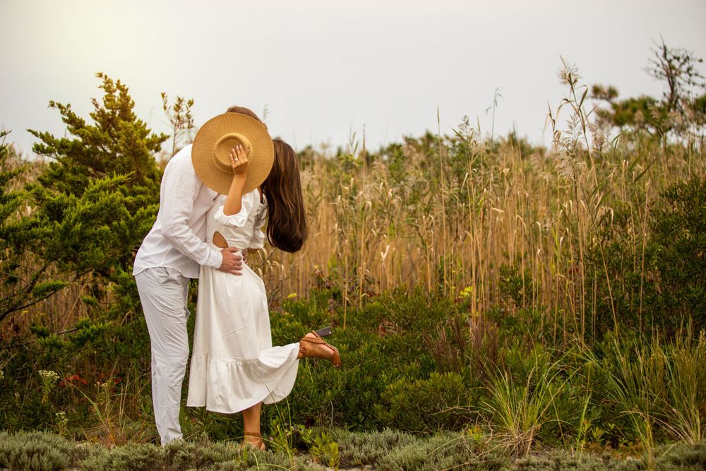 Engaged couple in white with hat in beach grass field Robert Moses Boardwalk