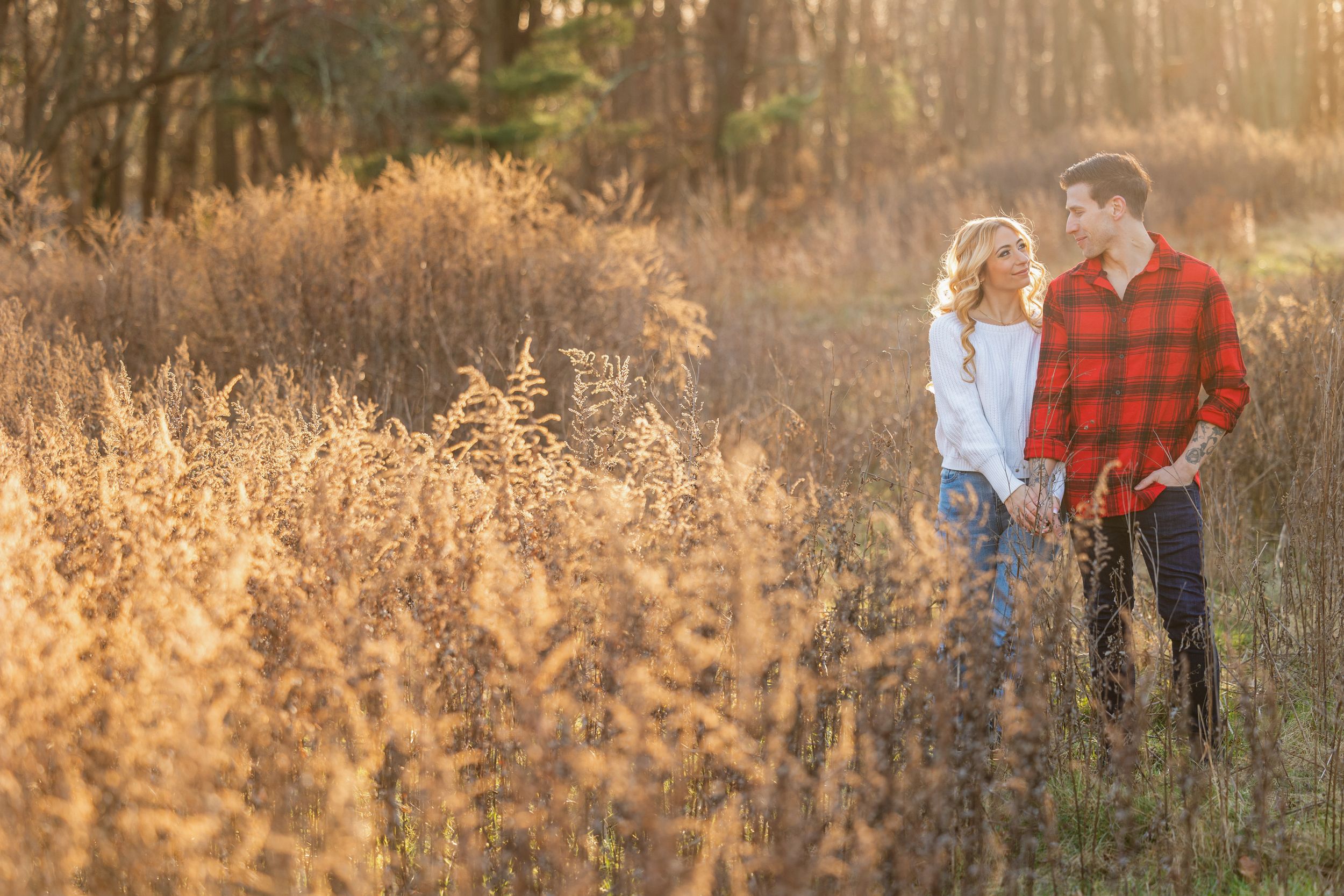 Romantic couple standing together in a golden field of tall grass at sunset.