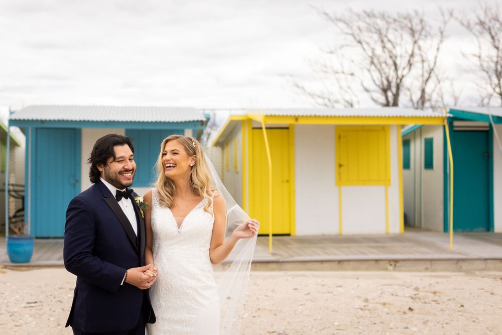 Couple poses in front of colorful beach cabanas during wedding photoshoot.