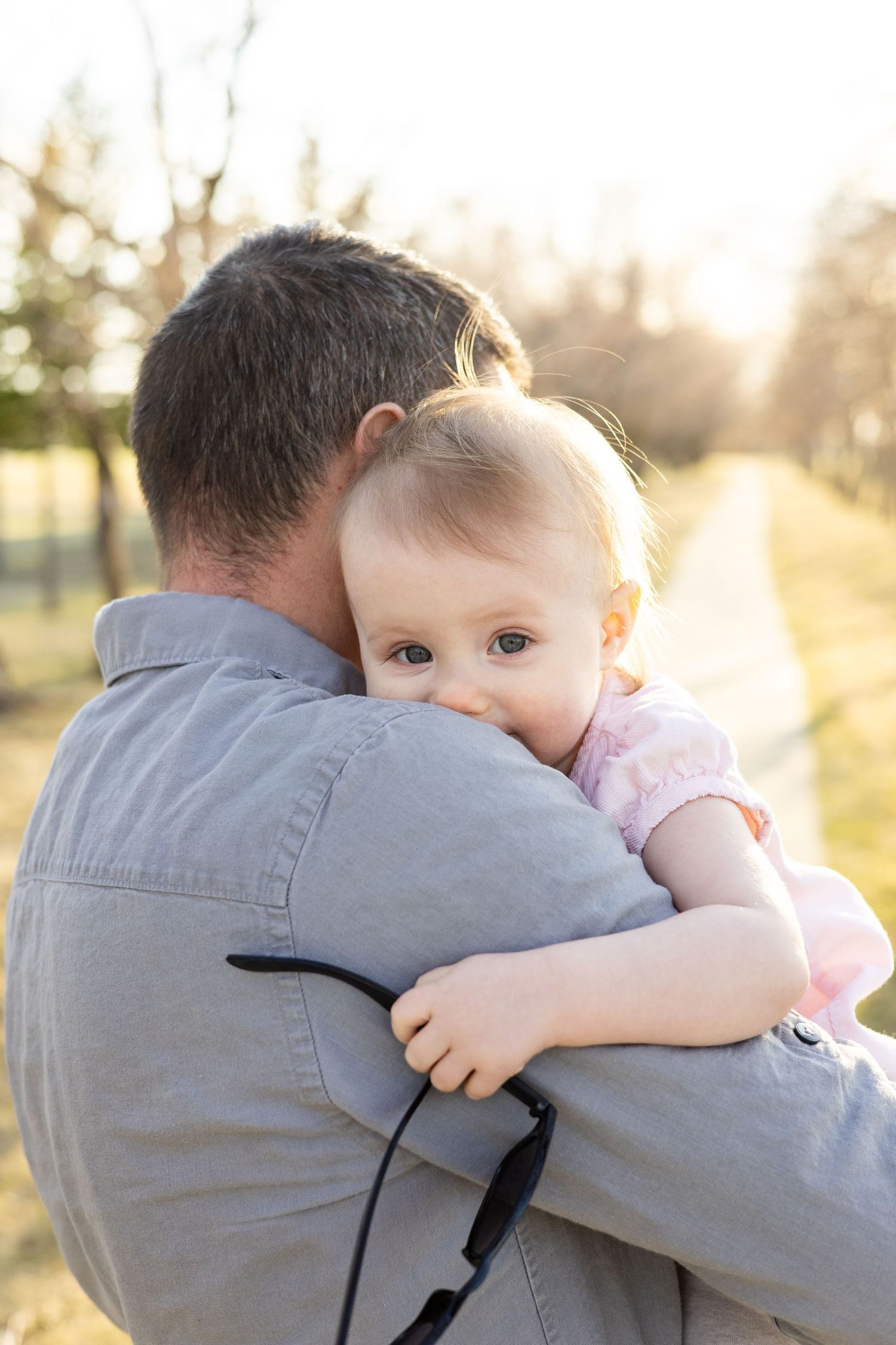 A tender moment captured between a young child and adult hugging in soft sunlit outdoor setting.