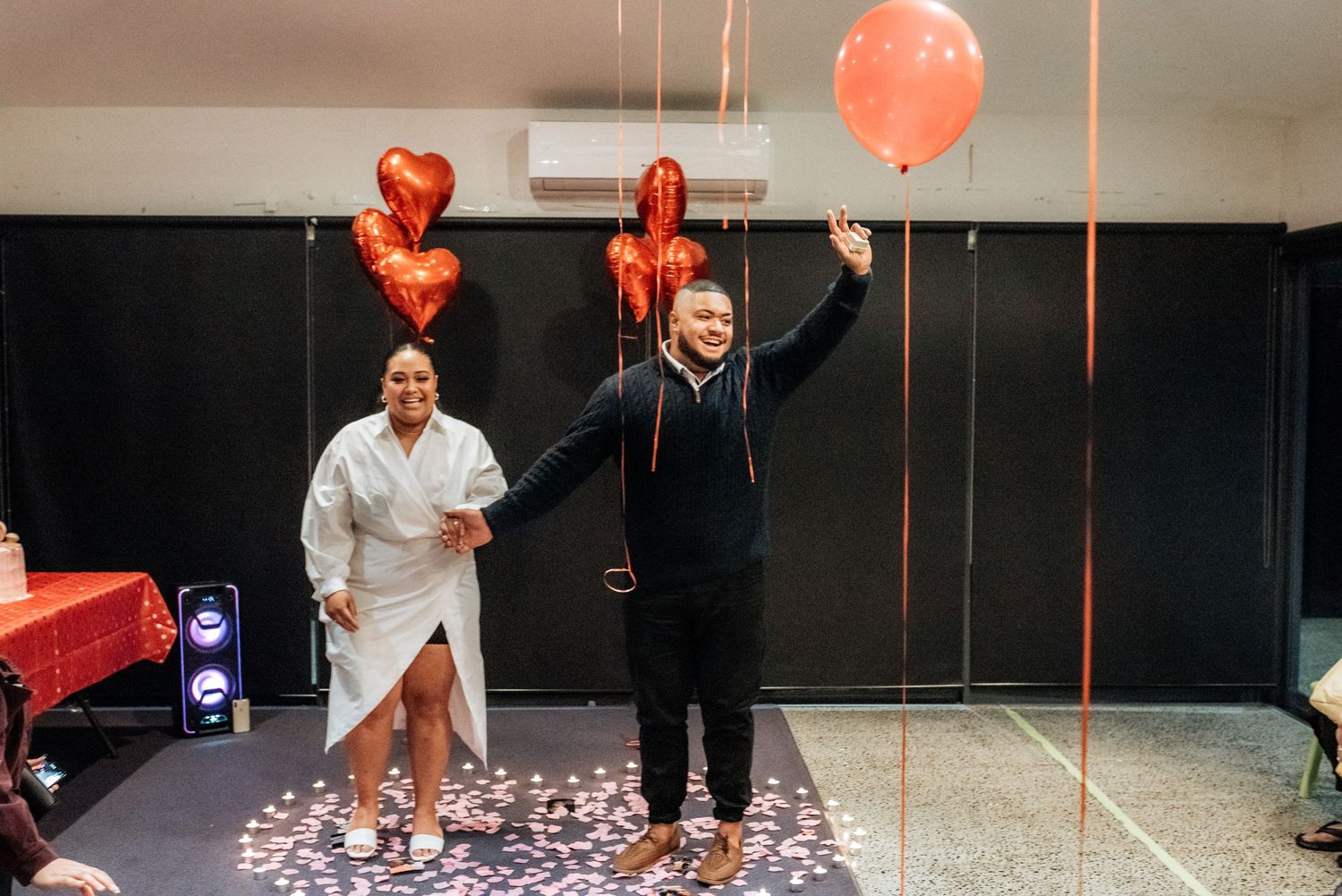 Joyful couple celebrate with red heart balloons and rose petals on a decorated dance floor.