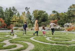 A group walks together through a winding garden labyrinth path surrounded by autumn foliage and trees.