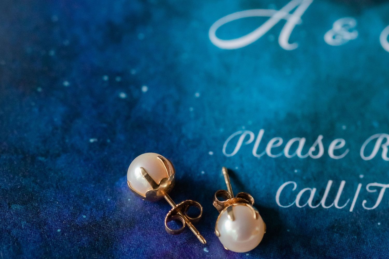 Pearl earrings and wedding stationery details on a deep blue background.