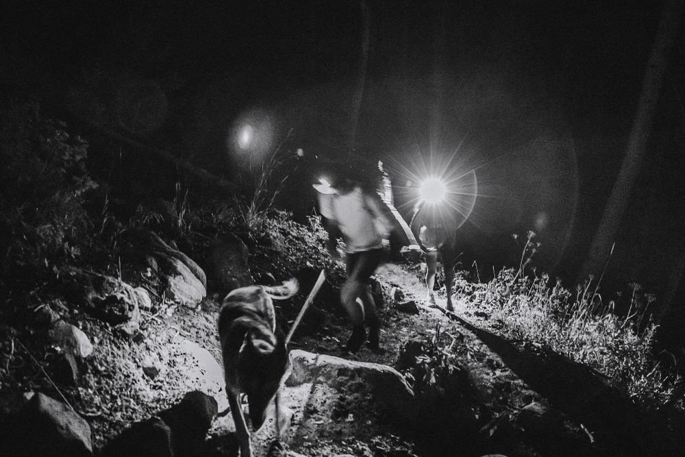 Night hiking scene illuminated by headlamps in grassy terrain.