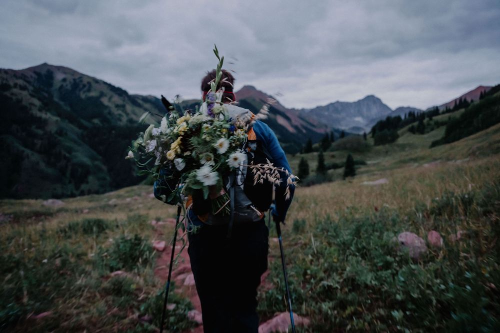 Hiker carrying floral arrangements in backpack against mountain backdrop.