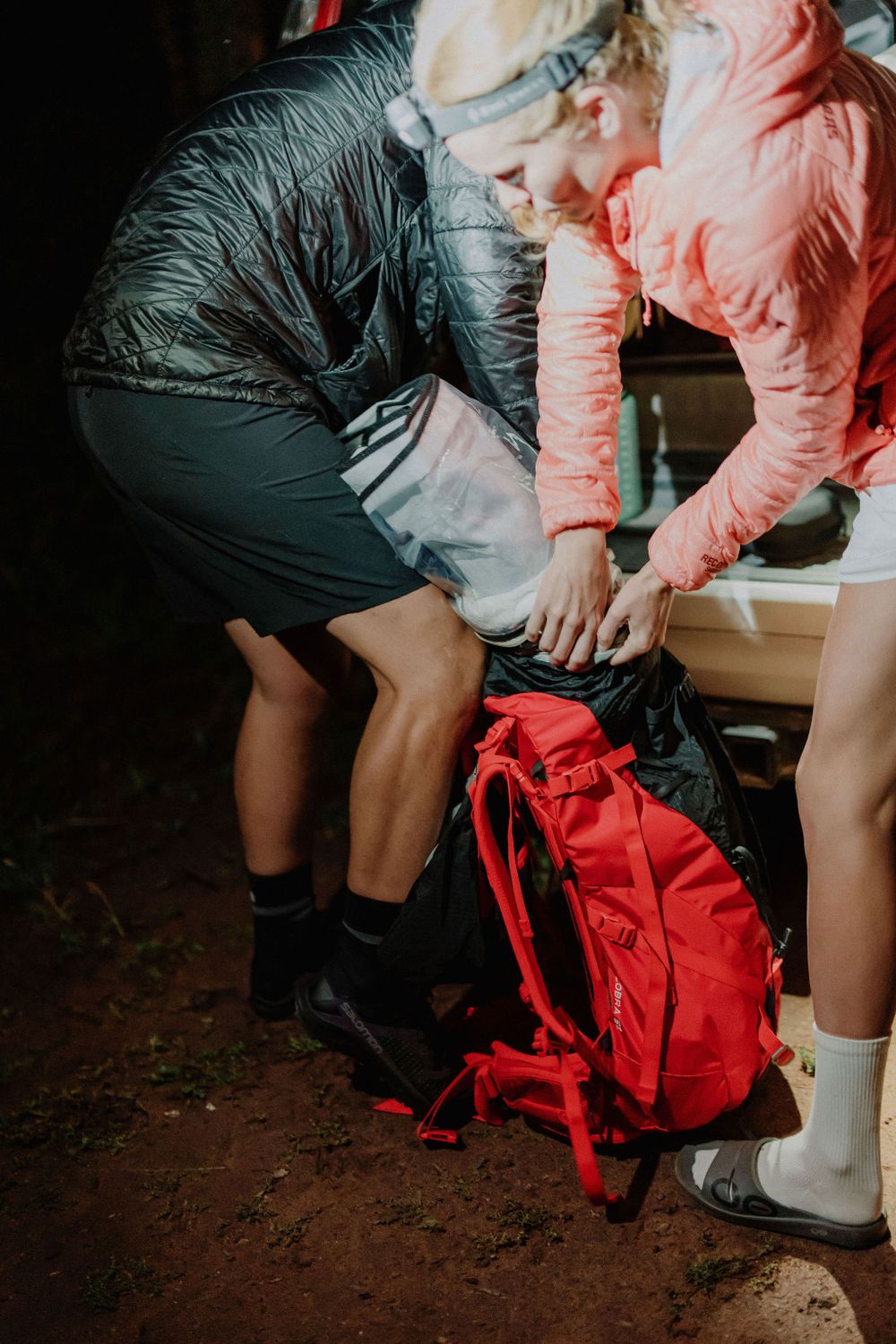 Hikers packing gear into backpack on outdoor trail.