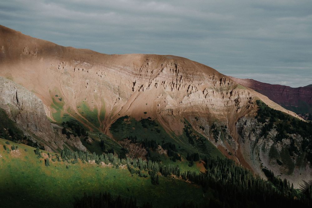 Dramatic mountain ridge catches evening light against moody sky in alpine landscape.