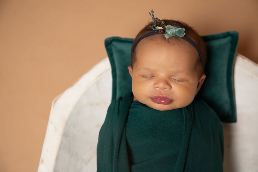 Close-up of smiling newborn in emerald wrap against white bowl backdrop.