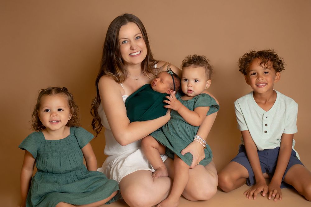 Family portrait against brown backdrop with children in matching green outfits and white attire.