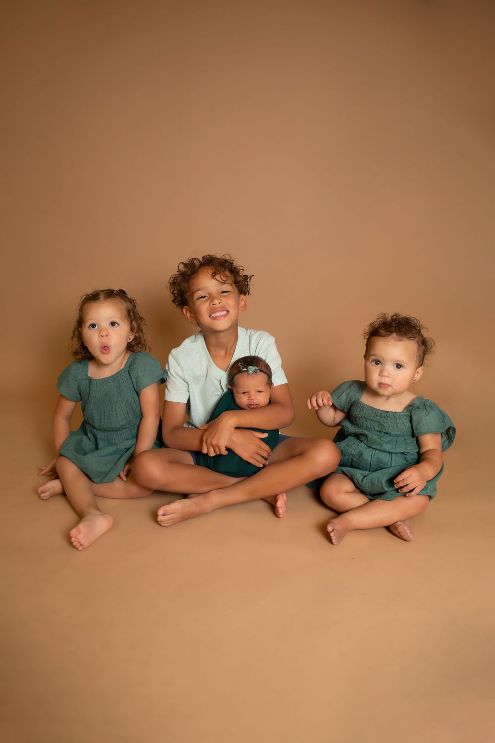 Playful sibling portrait with children in matching outfits against brown backdrop.