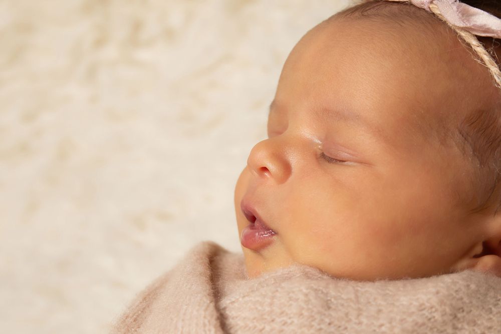 Peaceful sleeping baby swaddled in soft beige blanket with pink headband.