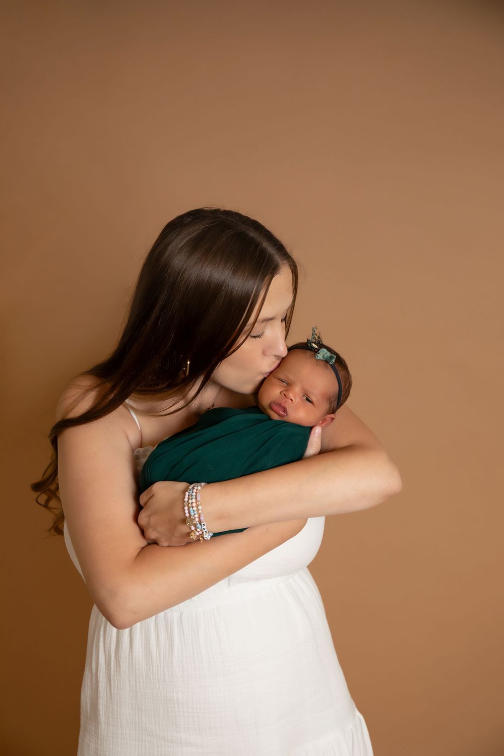 Tender moment between mother and sleeping newborn against warm brown background.