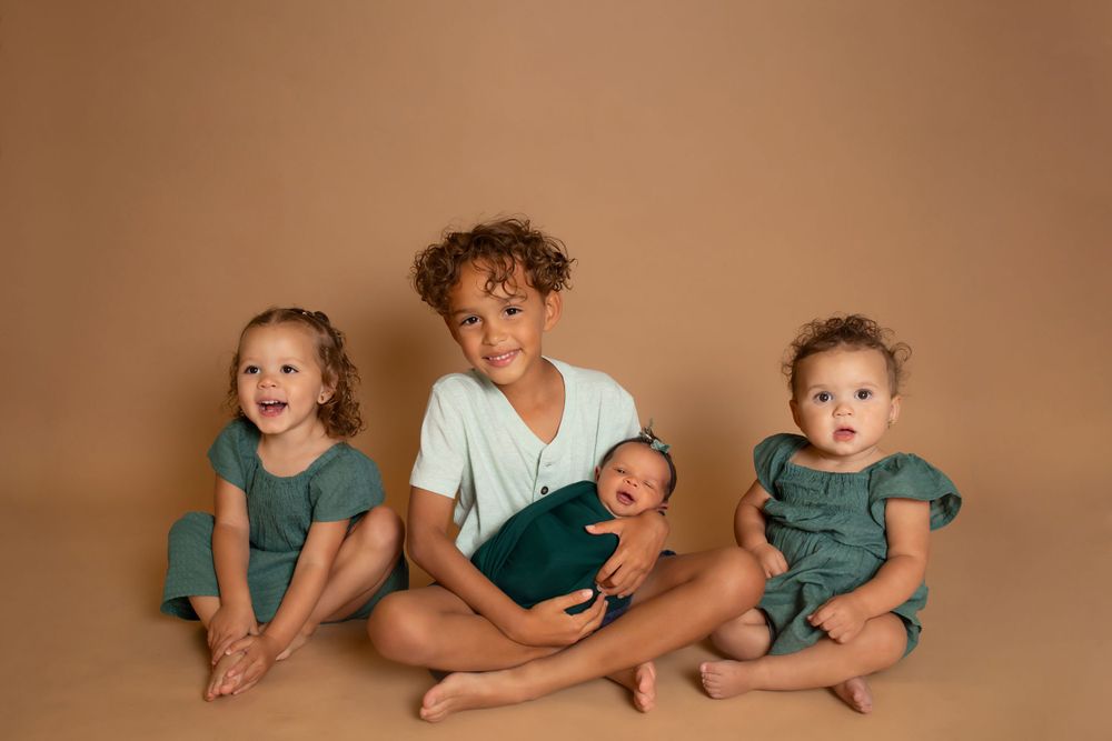 Children sitting together on brown background in coordinated green and white outfits.