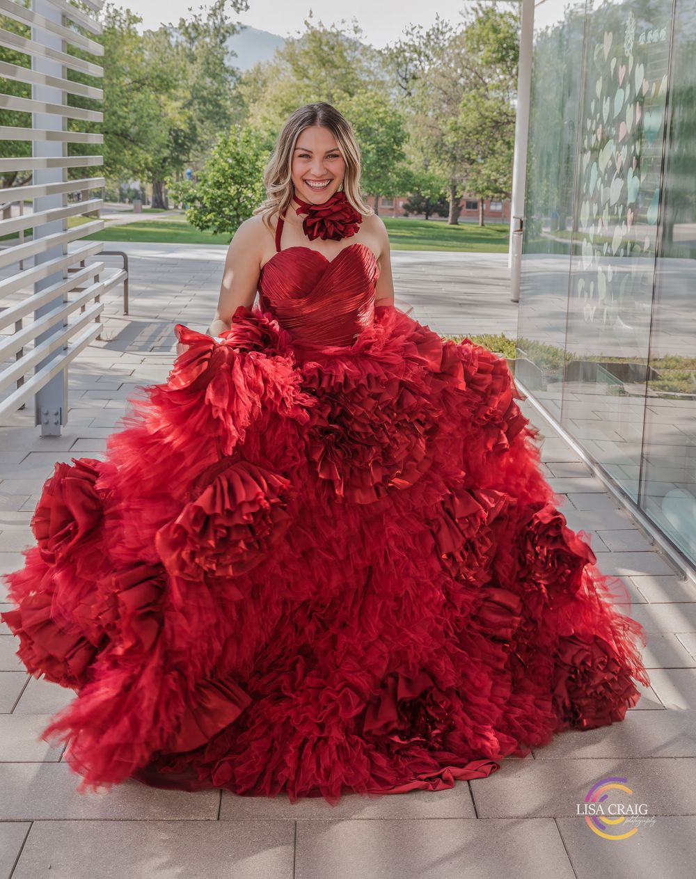 Person in dramatic red ruffled ball gown posed on outdoor terrace.