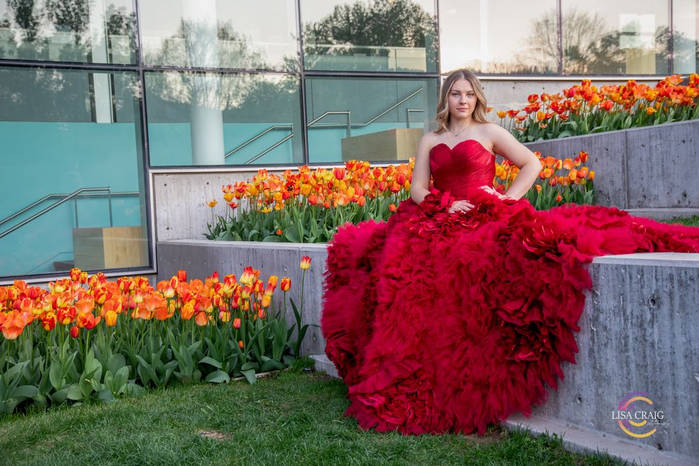 A dramatic red ball gown with ruffled layers photographed next to vibrant orange tulips in a garden setting.  Senior Portrait Photographer
