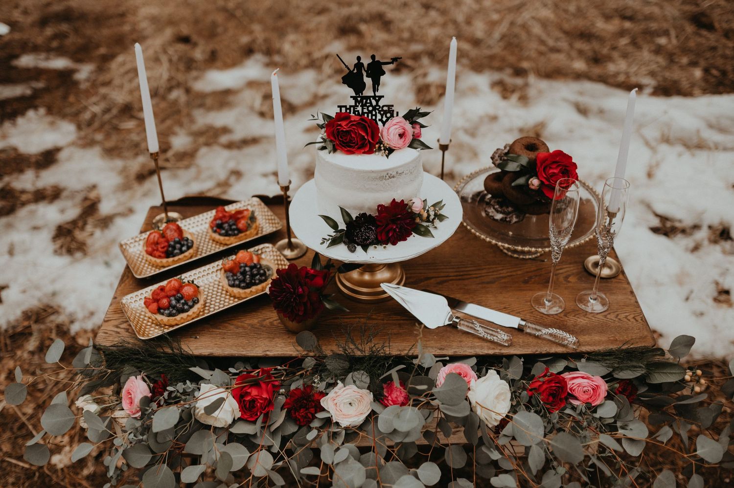Rustic outdoor table setting with red flowers and plates in a snowy winter scene.