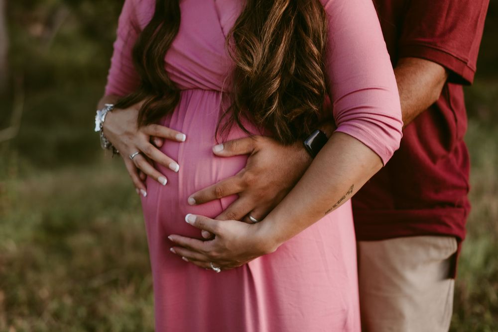 Hands rest lovingly on pregnant belly in pink maternity dress.