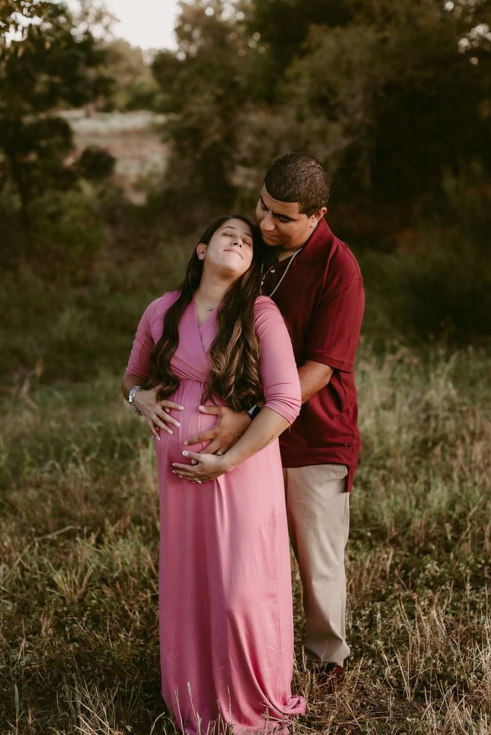 Close-up of expecting couple sharing tender moment outdoors in pink and burgundy.