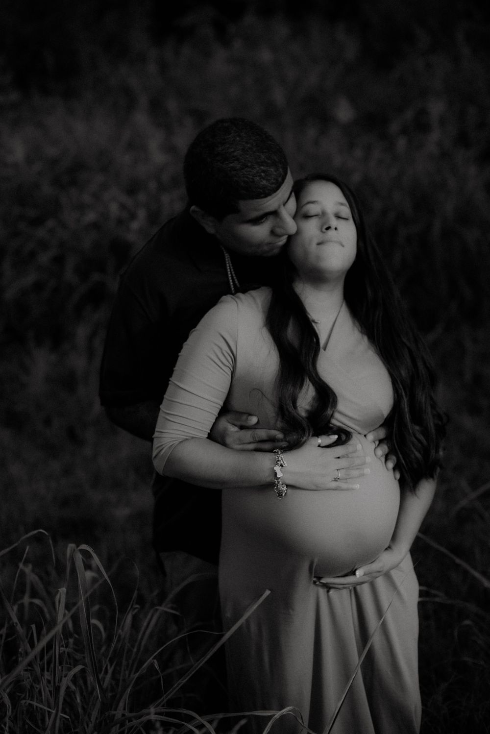 Black and white intimate maternity photo of couple embracing in tall grass.