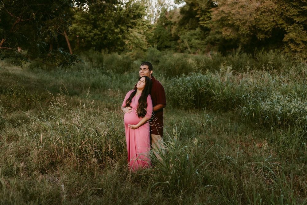 A couple embraces in a dreamy outdoor setting with tall grass and trees at sunset.