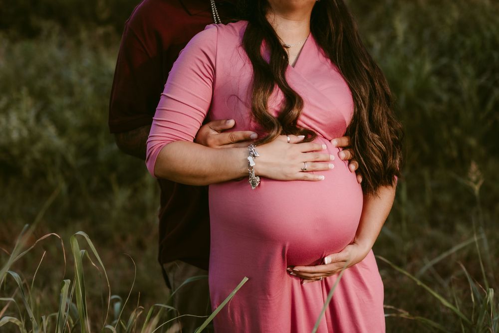 Close-up maternity photo showing hands cradling baby bump in pink dress.